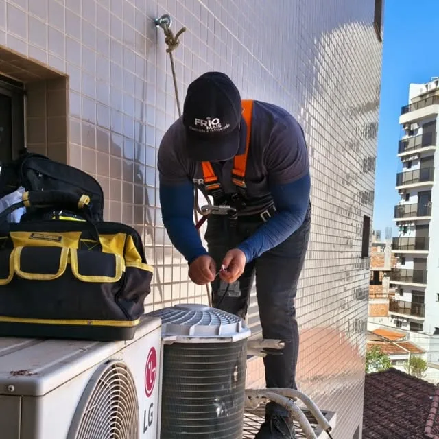 Técnico da Frio Mais com cinto de segurança instalando um aparelho na fachada de um prédio